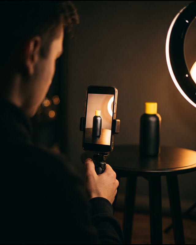 A creator films a skincare bottle on a phone under a ring light